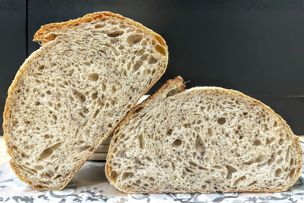 A round country sourdough boule with a scored, flour-dusted crust on a wooden board.